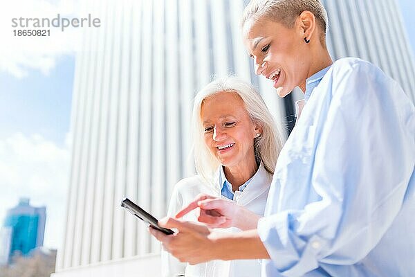 Frauen in Führungspositionen und Geschäftsfrauen in einem Geschäftsviertel  selbstbewusste Frauen lächelnd mit Blick auf ein Tablet