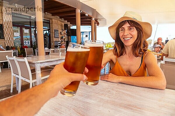 Rendezvous mit einer Freundin  die in einem Restaurant bei Sonnenuntergang am Strand mit Bier anstößt