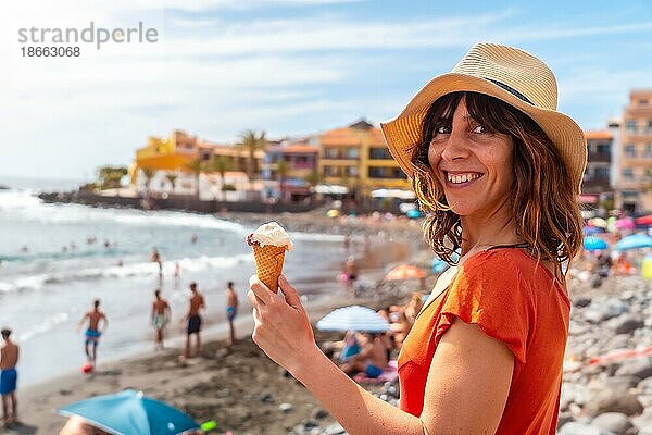 Lächelnde Touristin mit Hut isst ein Eis am Strand im Sommer am Strand von Valle Gran Rey auf La Gomera  Kanarische Inseln
