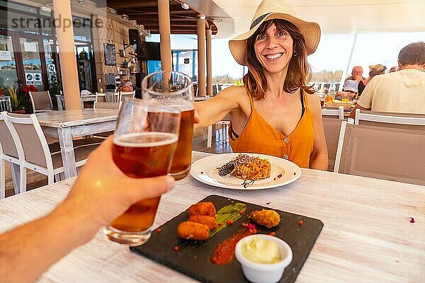 Rendezvous mit einer Freundin in einem Restaurant beim Abendessen am Strand im Urlaub bei Sonnenuntergang  Meeresfrüchte essen und darauf anstoßen