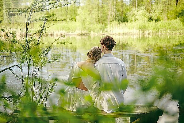 Junge Frau und ihr Mann sitzen auf einer Bank am Flussufer  sie schaut ihn zärtlich an