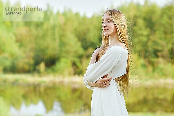 Schöne Frau in weißem Kleid am Flussufer mit verschränkten Armen