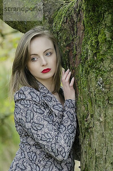 Nachdenkliche junge Frau lehnt an einem Baum und schaut weg