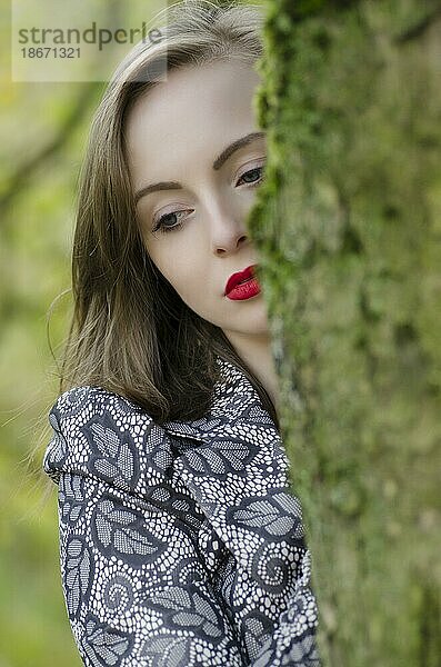 Nachdenkliche junge Frau hinter einem Baum stehend