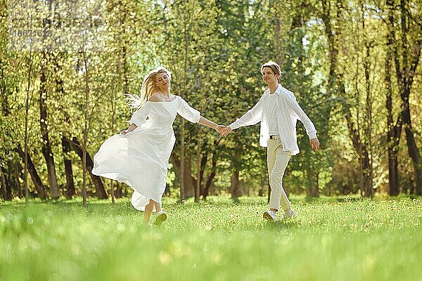 Glückliche Jungvermählte halten sich an den Händen und tanzen auf dem Rasen in der Sonne