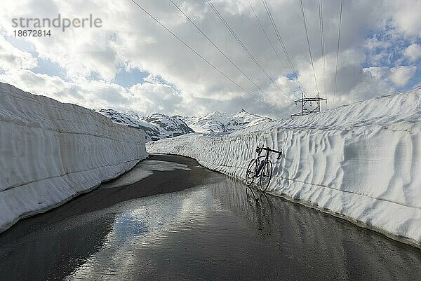 Fahrrad an eine Schneewand gelehnt auf dem Pass San Gottardo  schneebedeckter Berg im Hintergrund  Uri  Schweiz  Europa