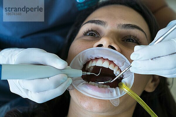 Die Zähne einer Frau werden in der Klinik behandelt. Ein Kieferorthopäde setzt mit zahnärztlichen Instrumenten eine Zahnspange auf die Zähne eines Patienten. Selektiver Fokus. Konzept der Zahnaufhellung  Zahnpflege  Mundgesundheit  Werbung für Zahnmedizin
