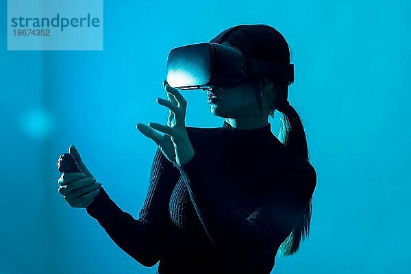 Metaverse Technologie Konzept. Frau in der virtuellen Realität VR Brille auf einem blauen Hintergrund. Futuristischer Lebensstil