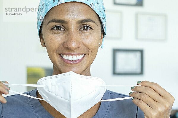 Schöne Ärztin lächelt in die Kamera  während sie ihre Maske abnimmt