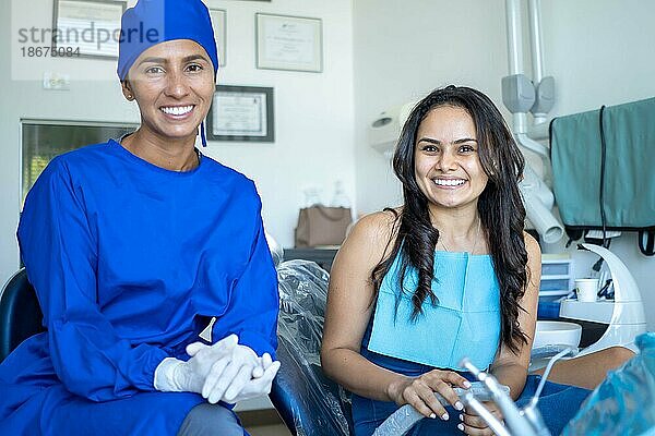 Lächelnde junge Frau bei zahnärztlicher Untersuchung mit ihrem Zahnarzt  beide schauen in die Kamera
