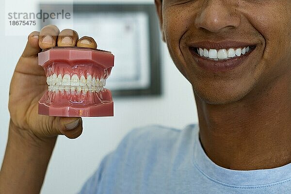 Nahaufnahme eines jungen Mannes  der eine Attrappe von Zähnen mit einem perfekten Lächeln zeigt. Konzept der Zahnaufhellung  Zahnpflege  Mundgesundheit  Werbung für Zahnmedizin