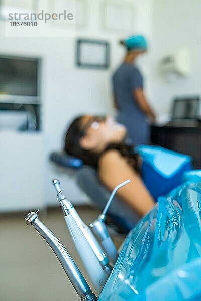 Zahnärztliche Werkzeuge und Geräte im Vordergrund und Patient und Zahnarzt unscharf im Hintergrund