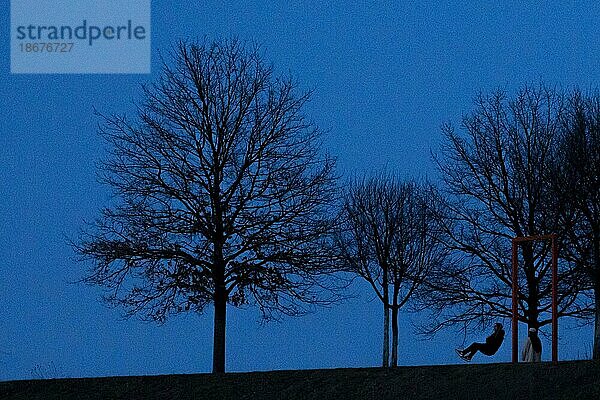 Eine Person auf einer Schaukel zeichnet sich bei blaür Stunde als Silhouette ab  aufgenommen in Berlin  08.03.2021. Berlin  Deutschland  Europa