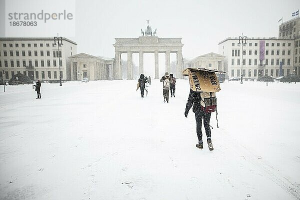 Berlin  Eine Person schützt sich mit einer Pappe  aufgenommen auf dem Pariser Platz vor dem Brandenburger Tor nach während starken Schneefalls in Berlin