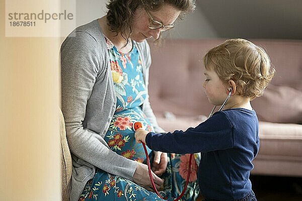 Thema: Familienplanung. Kind horcht mit einem Stethoskop am Bauch der schwangeren Mutter.  Bonn  Deutschland  Europa