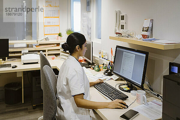 Seitenansicht einer Mitarbeiterin des Gesundheitswesens bei der Arbeit mit einem Desktop-PC im Krankenhaus