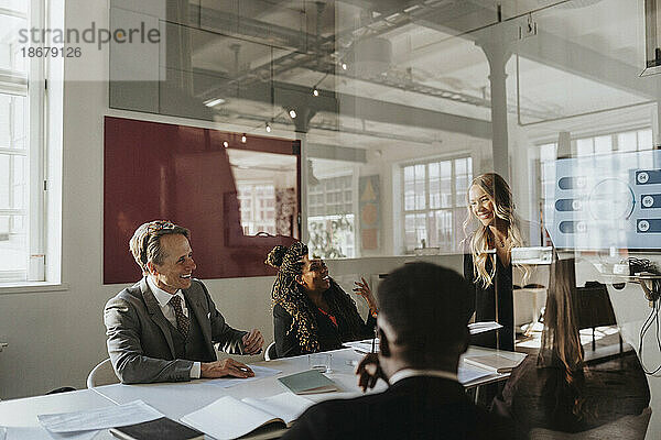 Glückliche männliche und weibliche Unternehmer bei einem Geschäftstreffen im Büro  gesehen durch Glas
