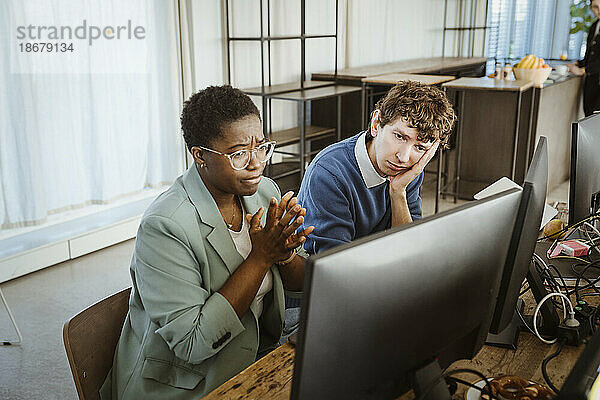 Angespannte männliche und weibliche Programmierer  die in einem kreativen Büro auf einen Computerbildschirm schauen