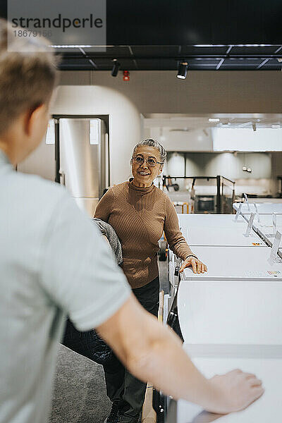 Ältere Frau diskutiert mit männlichem Verkäufer bei Waschmaschinen in einem Elektronikgeschäft