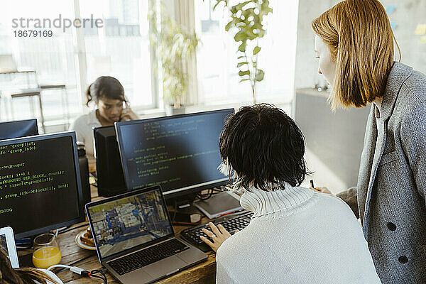 Manager diskutiert mit Programmierer über Computer am Schreibtisch im Büro