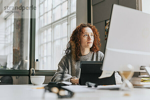 Konzentrierte rothaarige Geschäftsfrau  die im Büro an einem Desktop-PC arbeitet