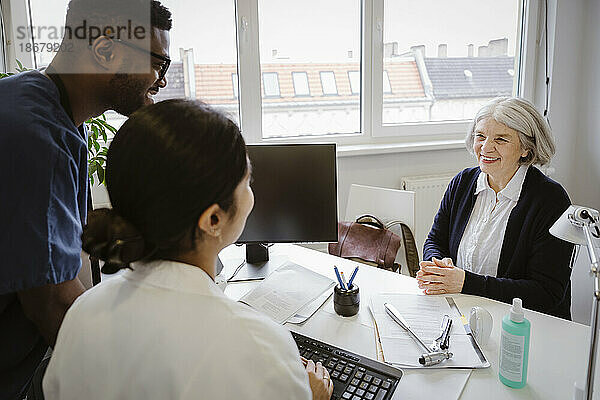 Lächelnder älterer Patient im Gespräch mit Ärzten am Schreibtisch in der Klinik