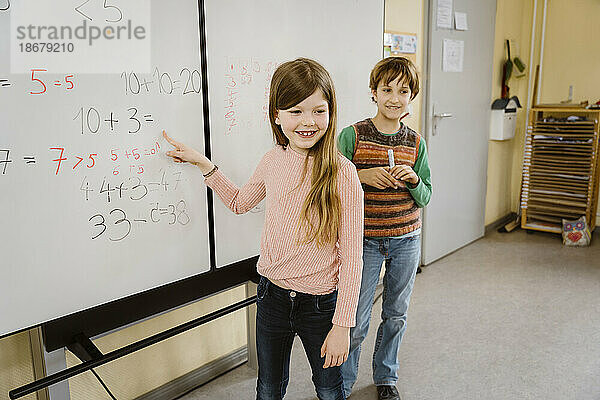Glückliches Mädchen  das mit einem Jungen im Klassenzimmer ein mathematisches Problem löst