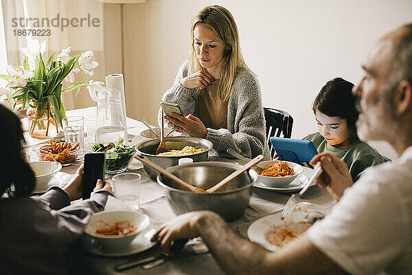 Familie benutzt Geräte  während sie am Esstisch sitzt