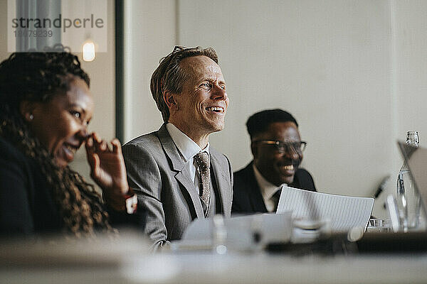 Lächelnder reifer Geschäftsmann  der während einer Sitzung im Sitzungssaal im Büro diskutiert