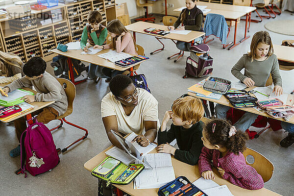 Lehrer erklärt männlichen und weiblichen Schülern  die im Klassenzimmer sitzen