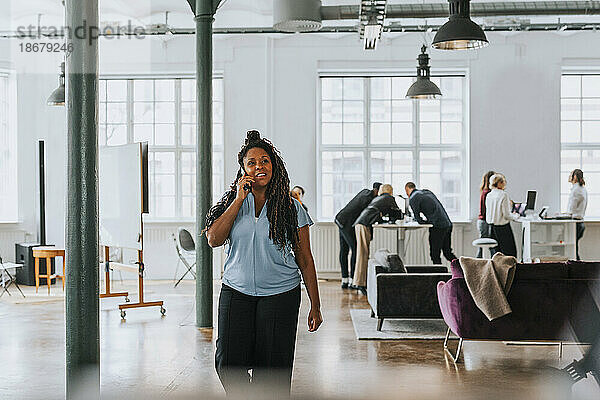 Nachdenkliche Geschäftsfrau  die beim Spazierengehen im Büro mit ihrem Smartphone telefoniert