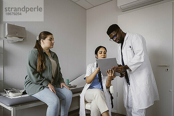 Männliche und weibliche Mitarbeiter des Gesundheitswesens besprechen sich über einen Tablet-PC mit einer Patientin in einer Klinik