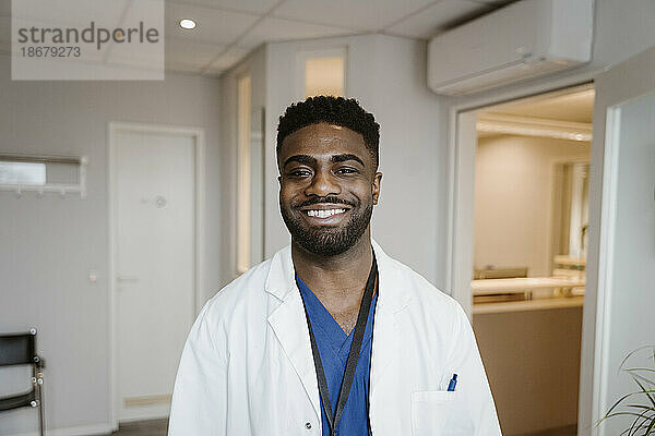 Porträt eines lächelnden jungen Arztes mit Laborkittel im Krankenhaus