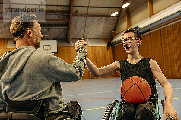 Fröhliche männliche und weibliche Athleten mit Behinderungen schütteln sich beim Basketballspielen auf dem Sportplatz die Hände