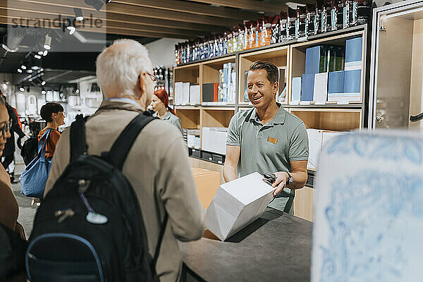 Ein lächelnder Verkäufer zeigt den Kunden an der Kasse eines Elektronikgeschäfts eine Gerätebox