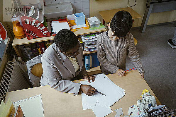 Hohe Winkel Ansicht der Lehrer hilft Jungen mit Diagramm am Schreibtisch im Klassenzimmer