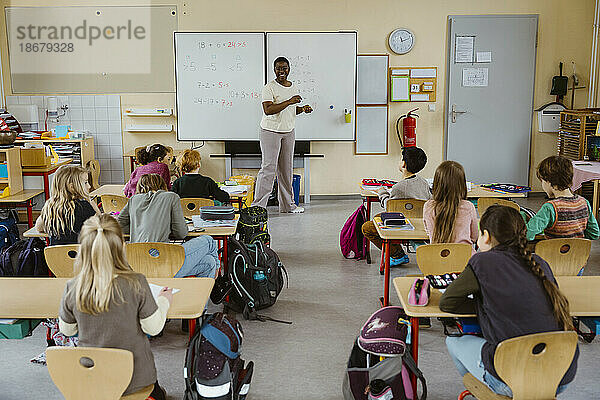 Glückliche Lehrerin steht vor der Tafel mit Schülern im Klassenzimmer