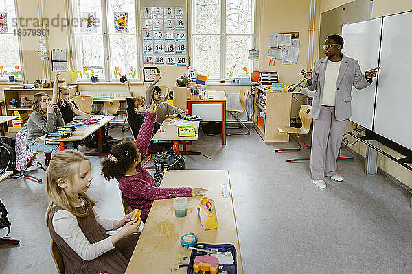 Lehrer  der an der Tafel steht und den Schülern im Klassenzimmer Fragen stellt