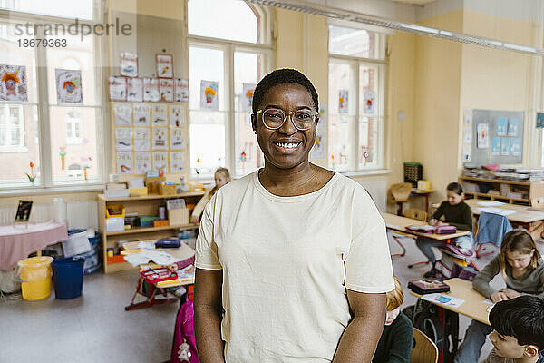 Porträt eines lächelnden Lehrers  der vor den Schülern im Klassenzimmer steht