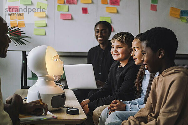 Lächelnde  gemischtrassige Studenten betrachten einen beleuchteten modernen Roboter im Innovationslabor