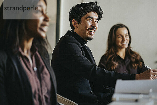 Lächelnder Geschäftsmann mit weiblichen Kollegen während einer Sitzung im Sitzungssaal im Büro