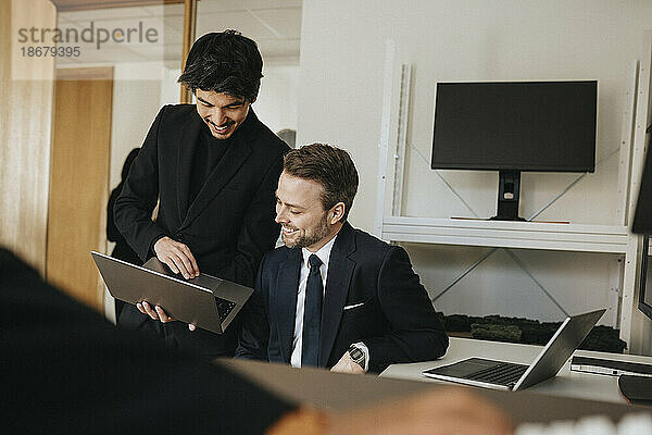 Lächelnder Geschäftsmann  der einem männlichen Kollegen im Büro seinen Laptop erklärt