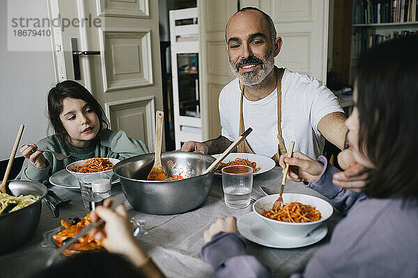 Glücklicher Vater isst Spaghetti mit Kindern am Esstisch