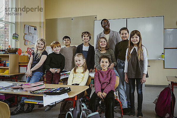 Porträt des lächelnden Lehrers und Jungen und Mädchen gegen Whiteboard im Klassenzimmer