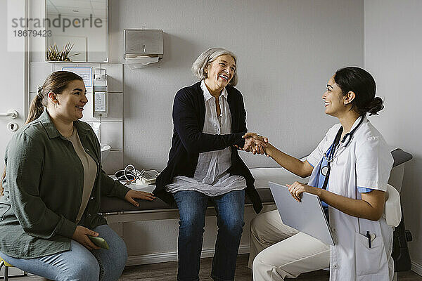 Glückliche ältere Frau schüttelt die Hand eines Arztes  der in einer Klinik sitzt