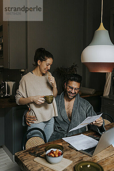 Lächelndes Paar beim Lesen eines Dokuments  während es zu Hause sitzt