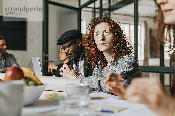 Rothaarige Geschäftsfrau sitzt mit Kollegen am Schreibtisch während einer Besprechung im Büro