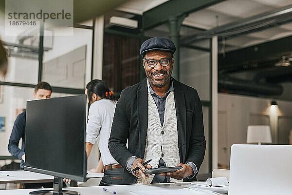 Porträt eines lächelnden Geschäftsmannes mit Tablet-PC  der an einem Schreibtisch im Büro steht