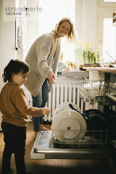 Glückliche Mutter und Sohn waschen zu Hause Geschirr in der Spülmaschine