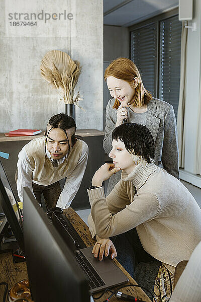 Lächelnde Geschäftsfrau mit Programmierern vor einem Computer in einem Startup-Büro